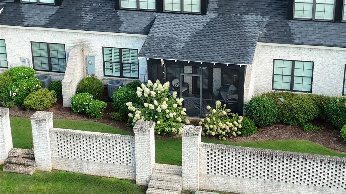 Lush landscaping frames a screened rear porch behind a low brick courtyard wall.