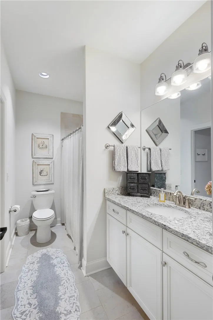 This guest bathroom has access to a bedroom as well as the foyer.  It features sleek stone countertops and a spacious vanity with chrome fixtures.