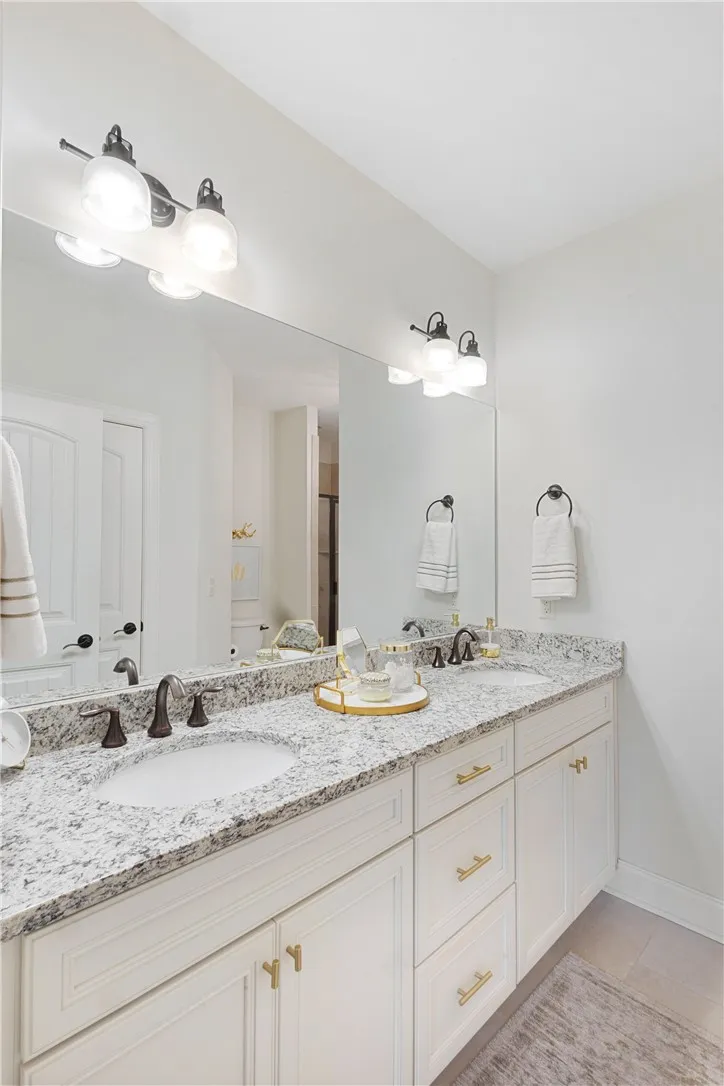 A spacious double vanity features granite countertops and sleek white cabinetry.