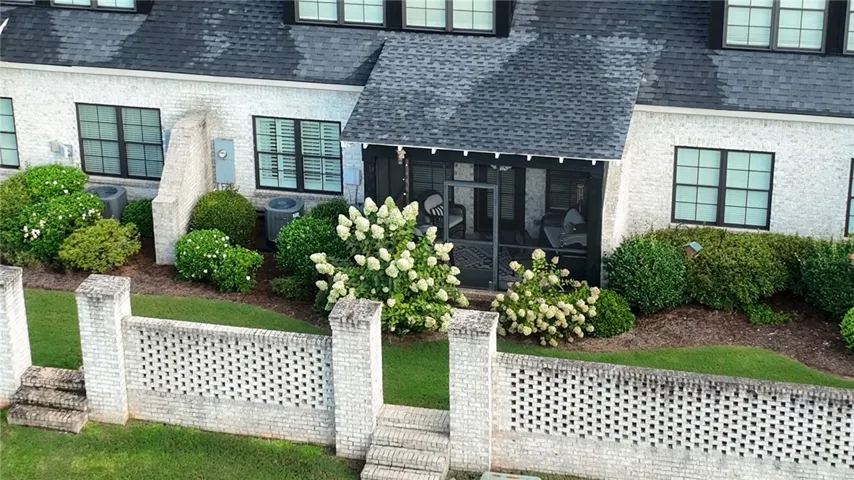 Lush landscaping frames a screened rear porch behind a low brick courtyard wall.