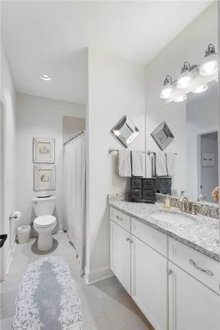 This guest bathroom has access to a bedroom as well as the foyer.  It features sleek stone countertops and a spacious vanity with chrome fixtures.
