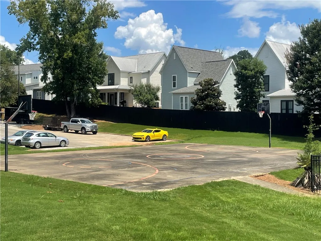 An outdoor basketball court and grassy yard are bordered by a privacy fence and residential homes.