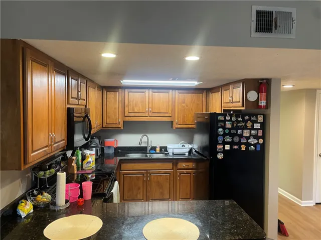 A compact kitchen featuring ample wood cabinetry, dark granite counters, and integrated appliances.