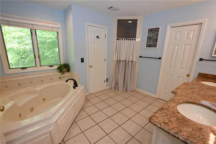 Primary en suite with jetted tub, linen closet, tiled shower, water closet, & double sink vanity.