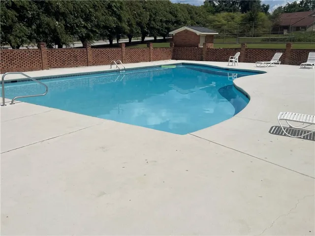 A spacious concrete deck surrounds this sparkling inground swimming pool enclosed by a brick wall.