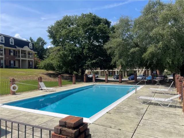 A sparkling swimming pool sits framed by mature trees and a gated enclosure.
