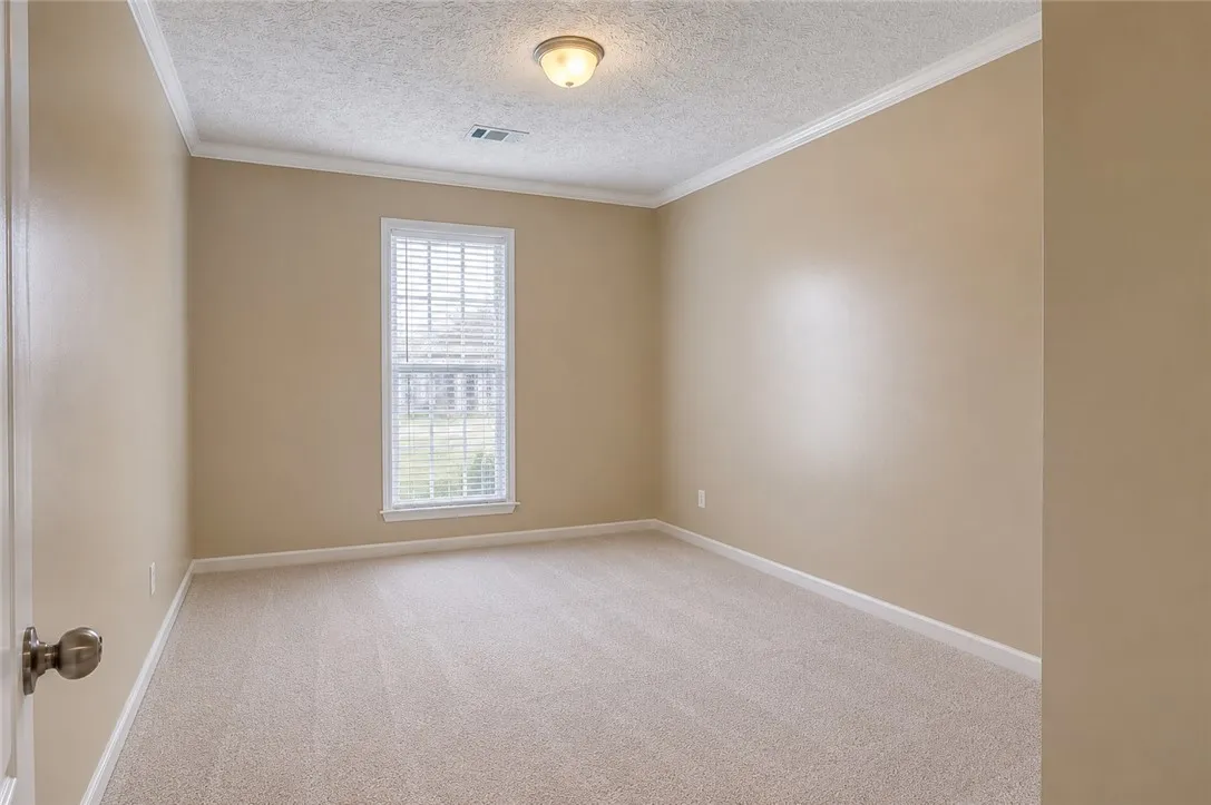 A well-lit bedroom provides a comfortable retreat with plush carpeting and a bright window.