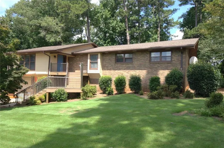 Mature trees frame a classic split-level brick exterior and manicured green lawn.