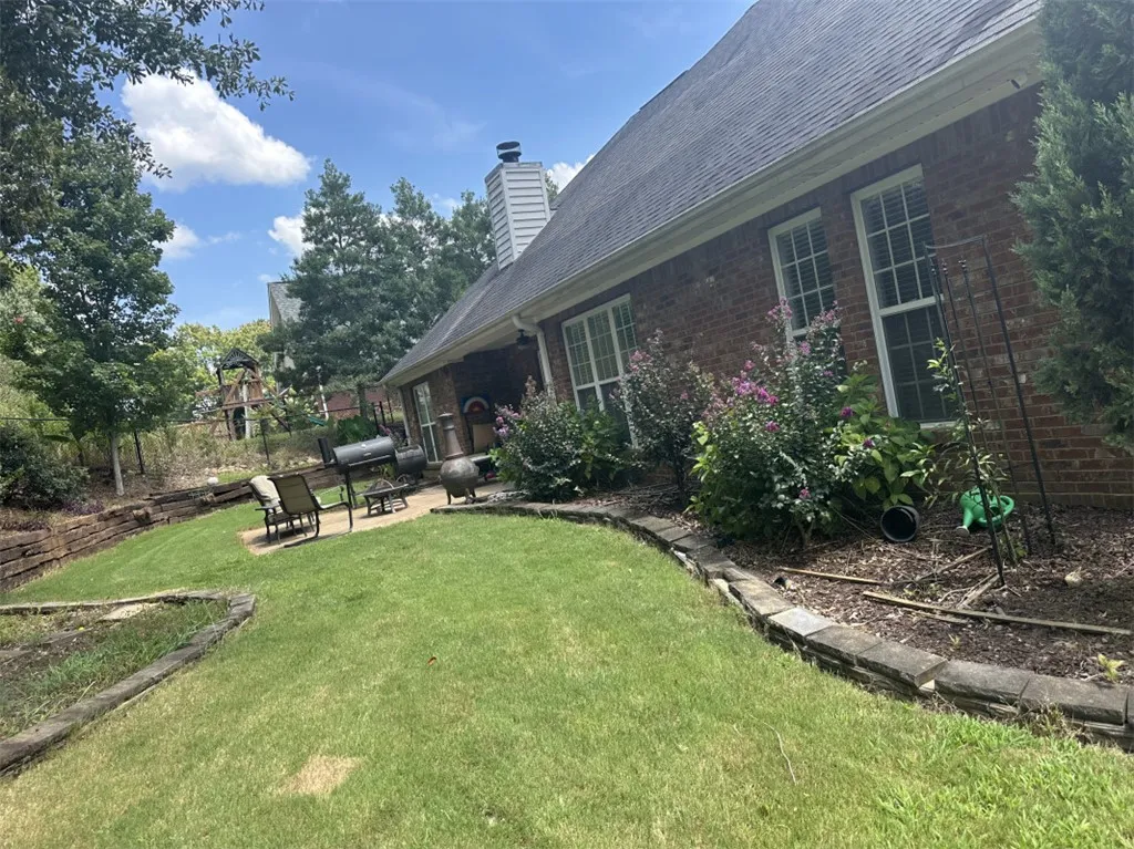Mature landscaping surrounds a brick exterior featuring a multi-tiered lawn and stone retaining walls.