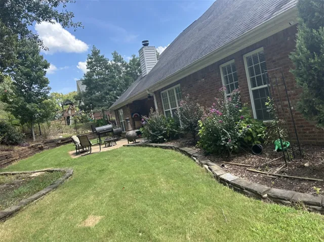 Mature landscaping surrounds a brick exterior featuring a multi-tiered lawn and stone retaining walls.