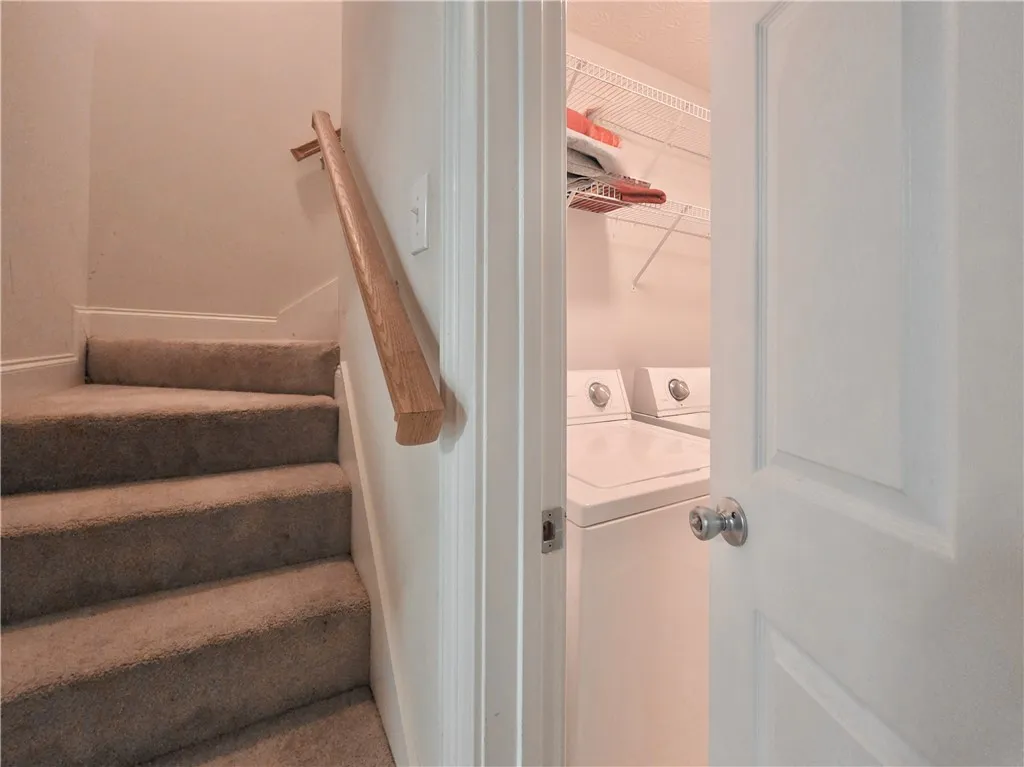 Carpeted stairs ascend beside a dedicated laundry room equipped with overhead shelving.