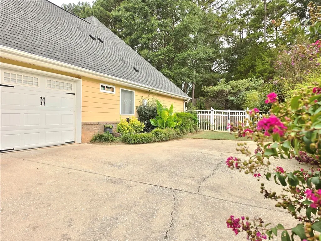 A spacious concrete driveway leads to an attached side-entry garage bordered by lush greenery.