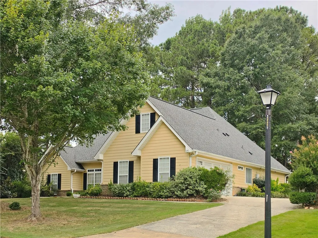 Mature trees frame a classic exterior featuring a paved driveway leading to the garage.