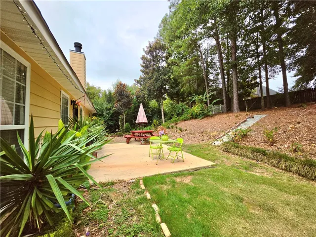 A spacious concrete patio overlooks a grassy backyard bordered by mature woodland trees.
