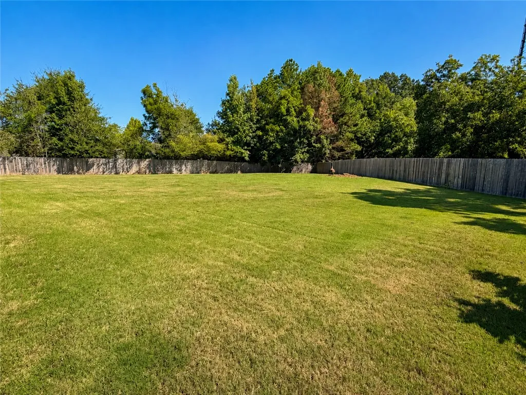 Mature trees frame a spacious, fully fenced lawn under clear blue skies.
