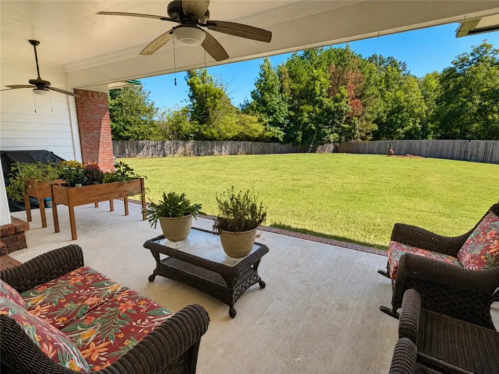 A spacious covered patio overlooks a large, wood-fenced grassy backyard bordered by mature trees.