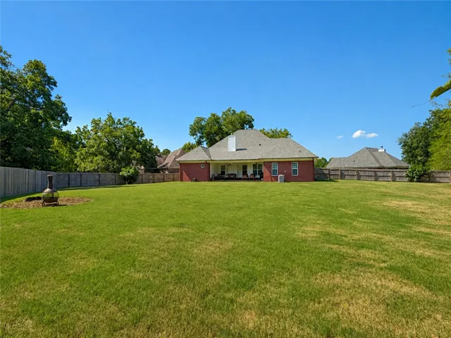 A spacious green lawn stretches out behind a classic brick home with a covered patio.