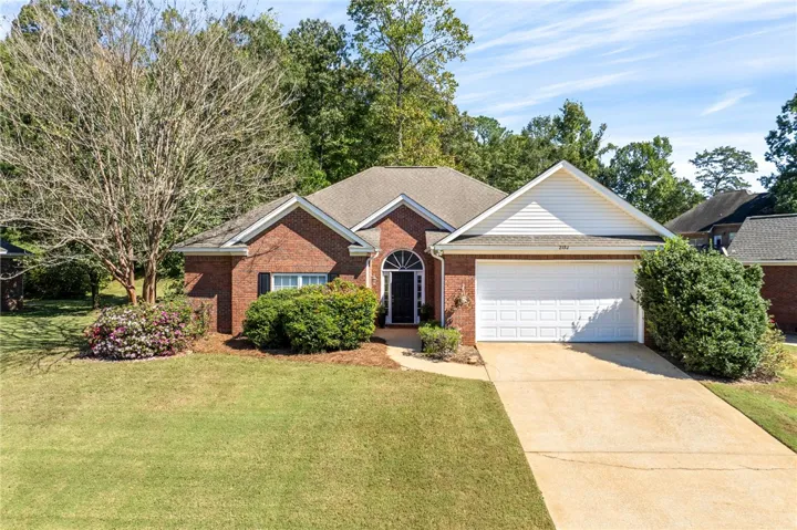 Mature trees frame a classic brick exterior complete with a two-car garage and manicured lawn.