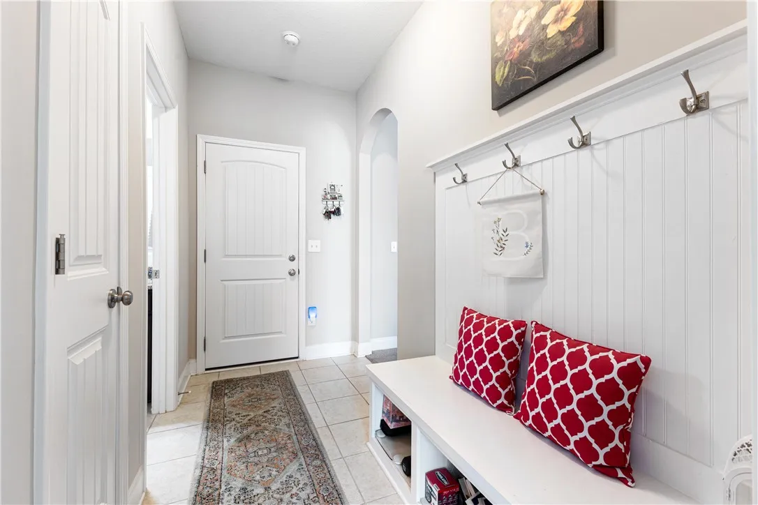 An inviting entryway by the garage door features a durable  bench, coat hooks and clean beadboard wainscoting.