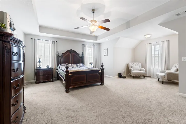 An airy bedroom highlights elegant tray ceilings and multiple windows for abundant natural light.