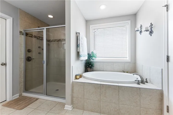 An oval soaking tub and a glass-enclosed shower feature neutral tile surrounds and recessed lighting.