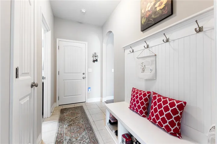 An inviting entryway by the garage door features a durable  bench, coat hooks and clean beadboard wainscoting.