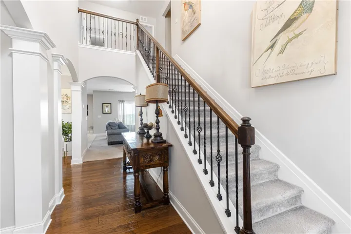 An elegant staircase with detailed wood railings and carpet runners ascends from the hardwood hallway.