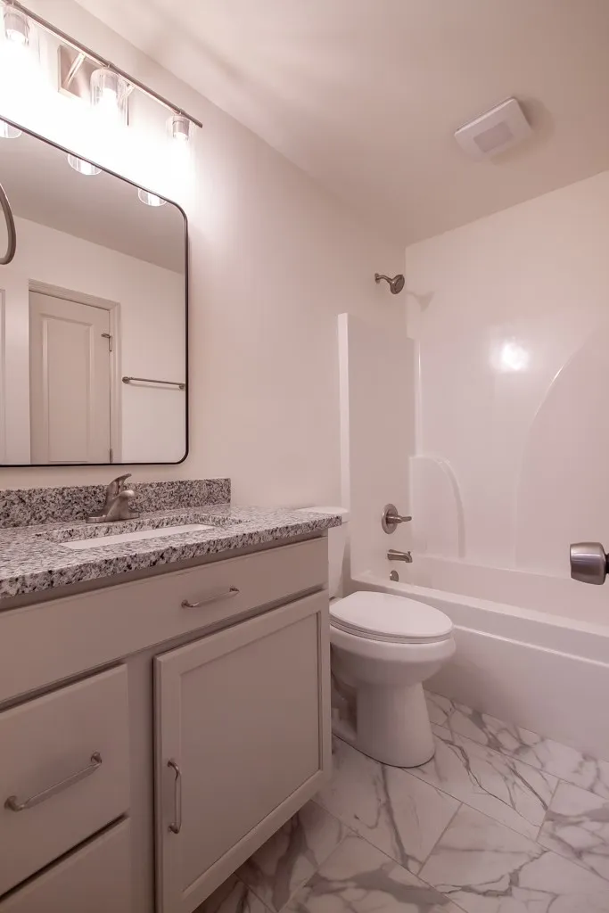 Polished stone counters and marble-patterned tile floors elevate this full bathroom.