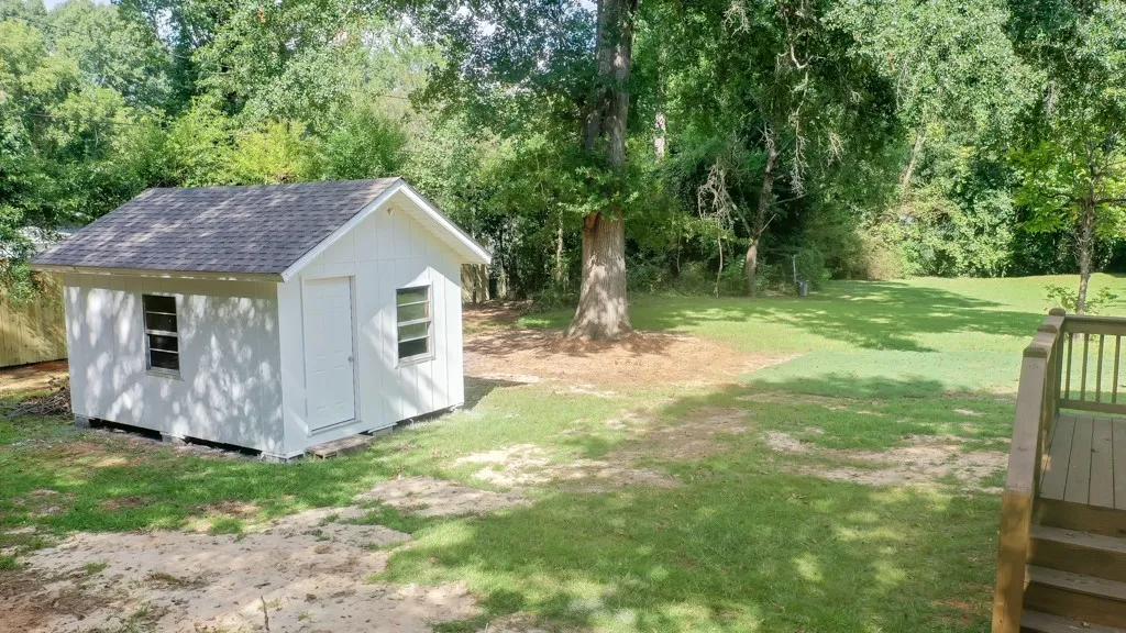 A spacious grassy yard features a freestanding storage shed and a wooden deck.