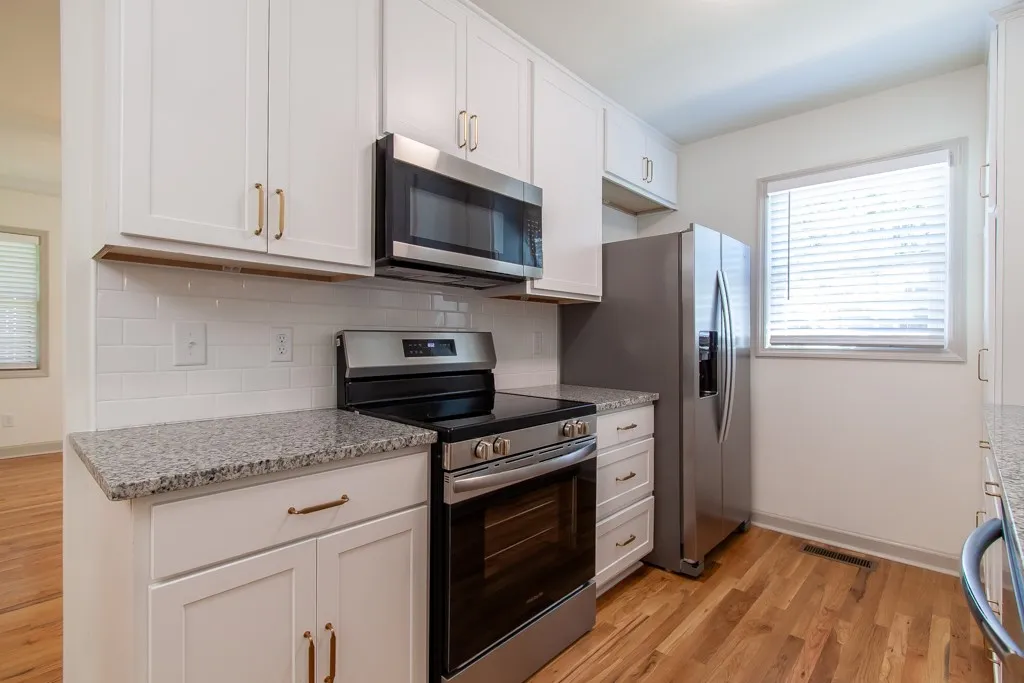 Polished stone countertops complement clean cabinetry and warm hardwood flooring in this kitchen space.