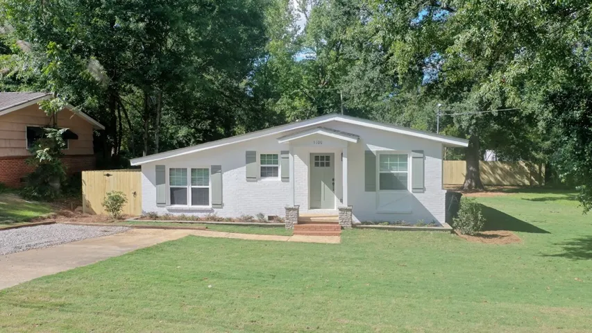 Mature trees frame a charming classic brick exterior nestled on a gentle grassy slope.