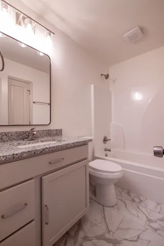 Polished stone counters and marble-patterned tile floors elevate this full bathroom.