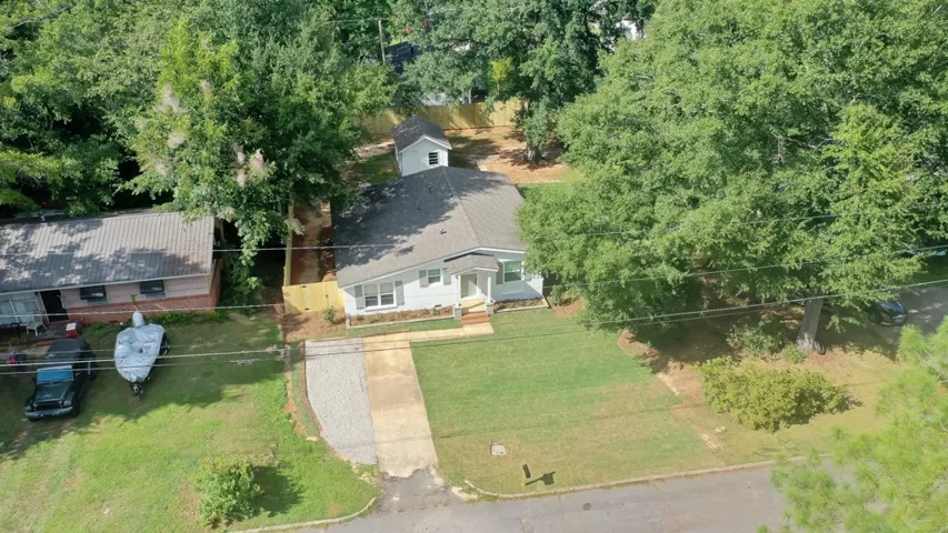 Mature trees frame a single-story home with a grassy lawn and detached outbuilding.
