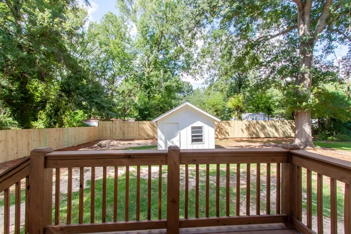 A spacious wooden deck overlooks the fenced grassy yard featuring a detached storage shed.