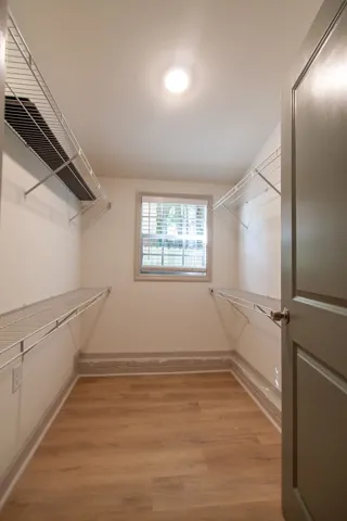 An organized walk-in closet boasts wood-style flooring and abundant wire shelving under a bright light fixture.