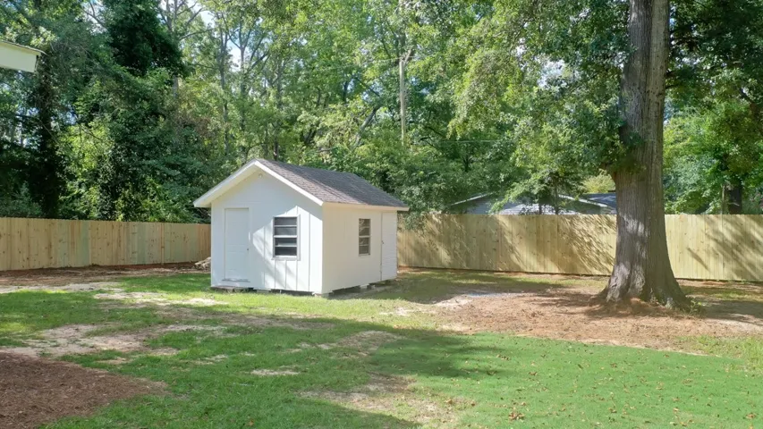 Mature trees shade a spacious backyard featuring a fully enclosed wooden fence and useful outbuilding.