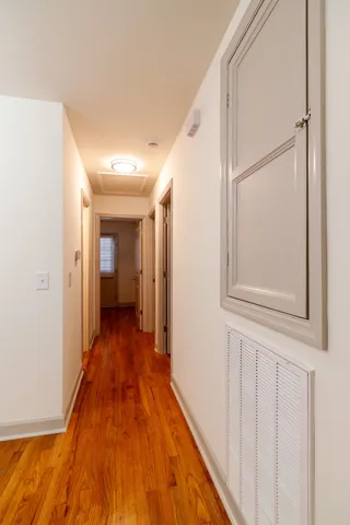 Gleaming hardwood floors run the length of a hallway featuring crisp white walls.