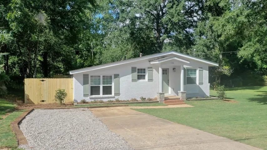 Mature trees frame a welcoming entrance porch and neat driveway at this single-level home.