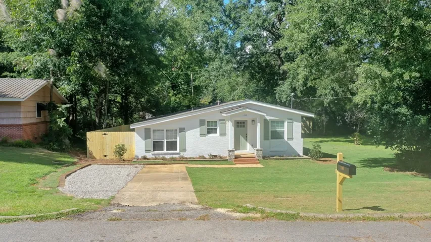 Mature trees frame a charming single-level brick home with a grassy lawn.