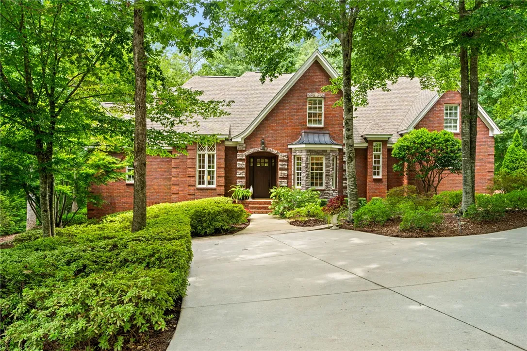 Mature trees frame a classic brick exterior with a welcoming driveway.