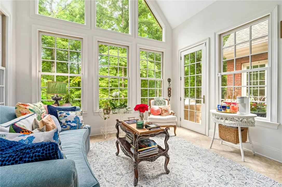 Towering windows frame tranquil wooded views in this light-filled sunroom connected to the primary suite.