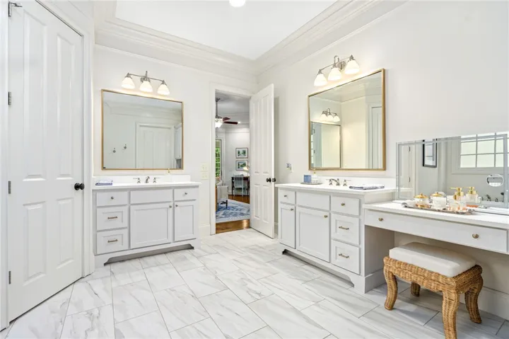 Crown molding and tiled floors elevate this spacious bathroom with dual vanities.