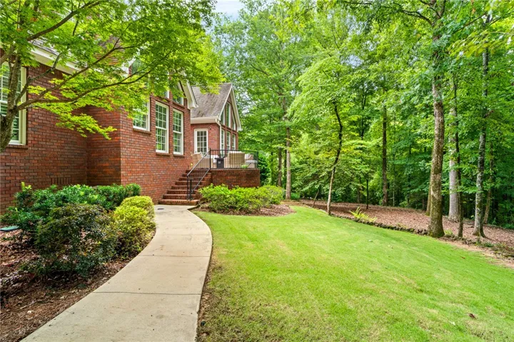 A curved concrete walkway leads alongside the brick exterior toward the wooded backyard.