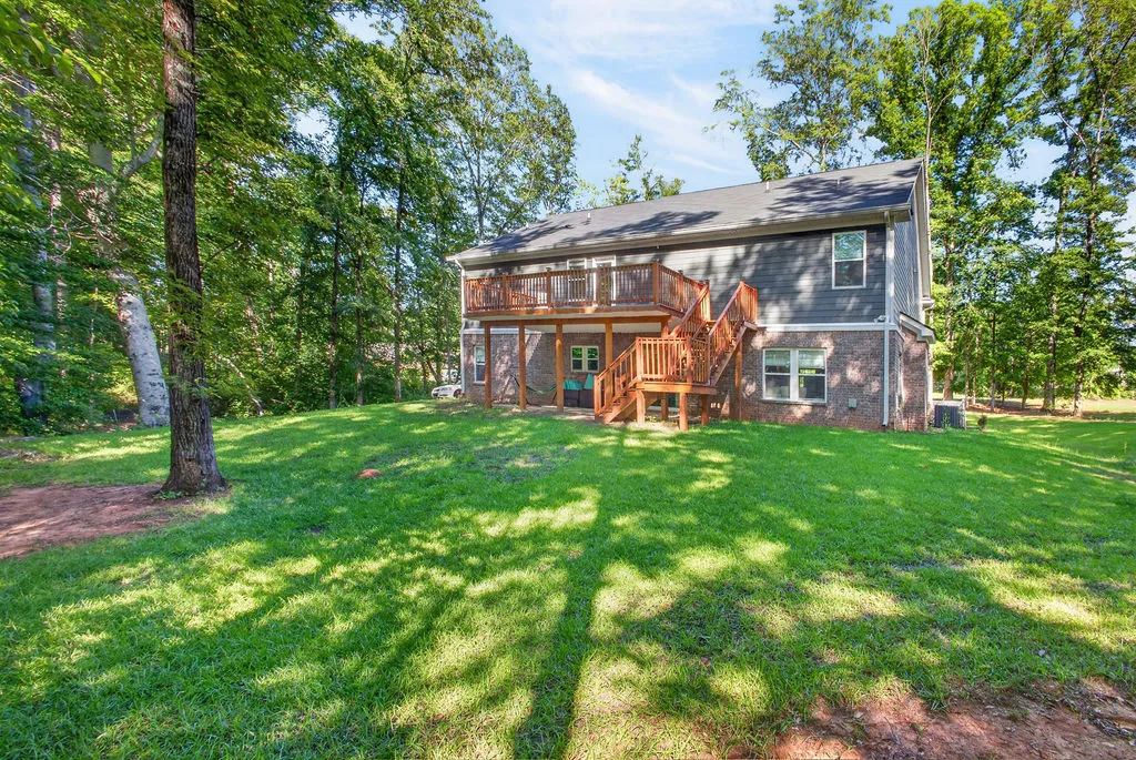 A spacious backyard with lush green grass, bordered by dense woods, featuring a multi-level deck and brick accents.