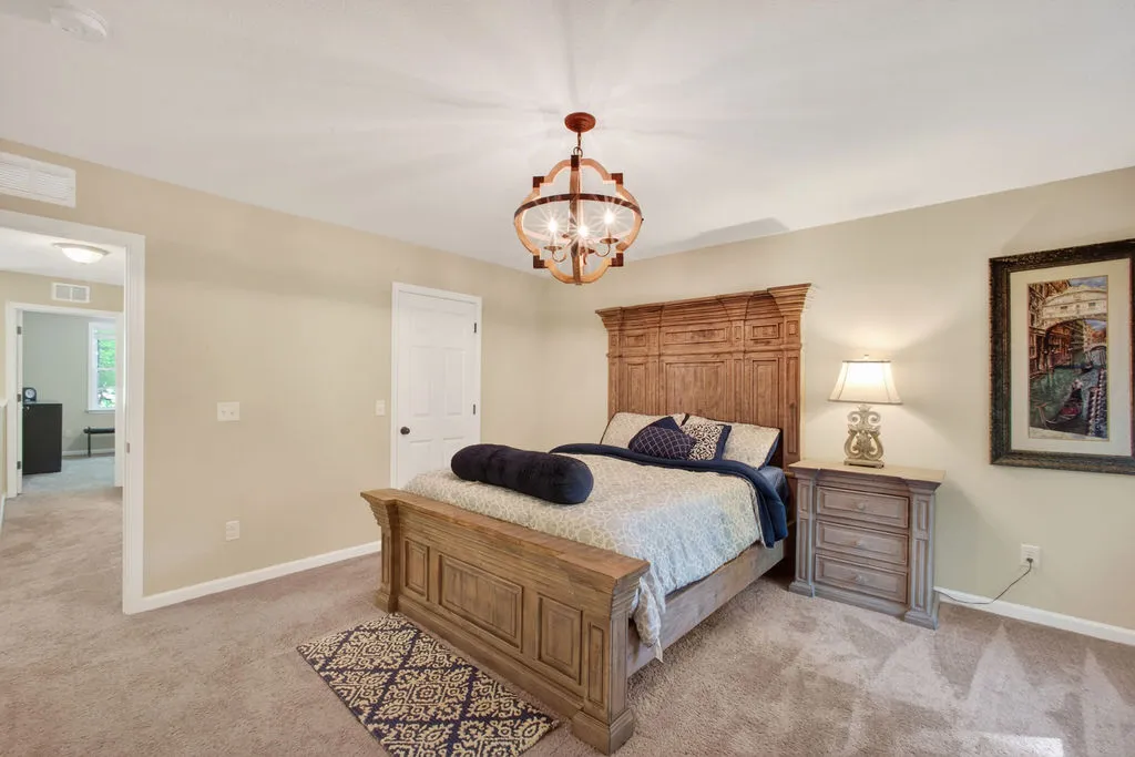 An inviting bedroom with plush carpeting features a striking wood bed frame and a charming chandelier.