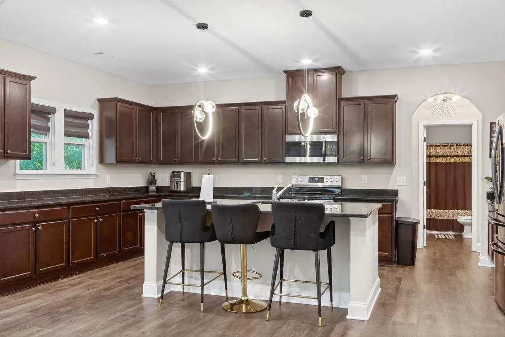 A contemporary kitchen features dark cabinetry, granite countertops, and modern pendant lighting over a breakfast bar.