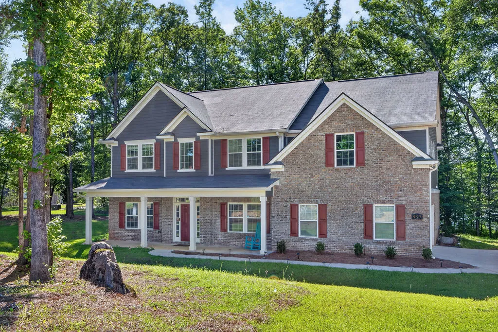 A classic brick and siding two-story home, nestled among a lush, mature tree canopy, features an inviting front porch.