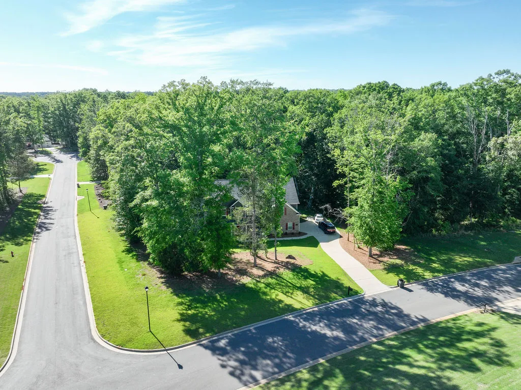 An aerial view showcases a welcoming home nestled amongst lush, mature trees, accessed via a long, paved driveway.