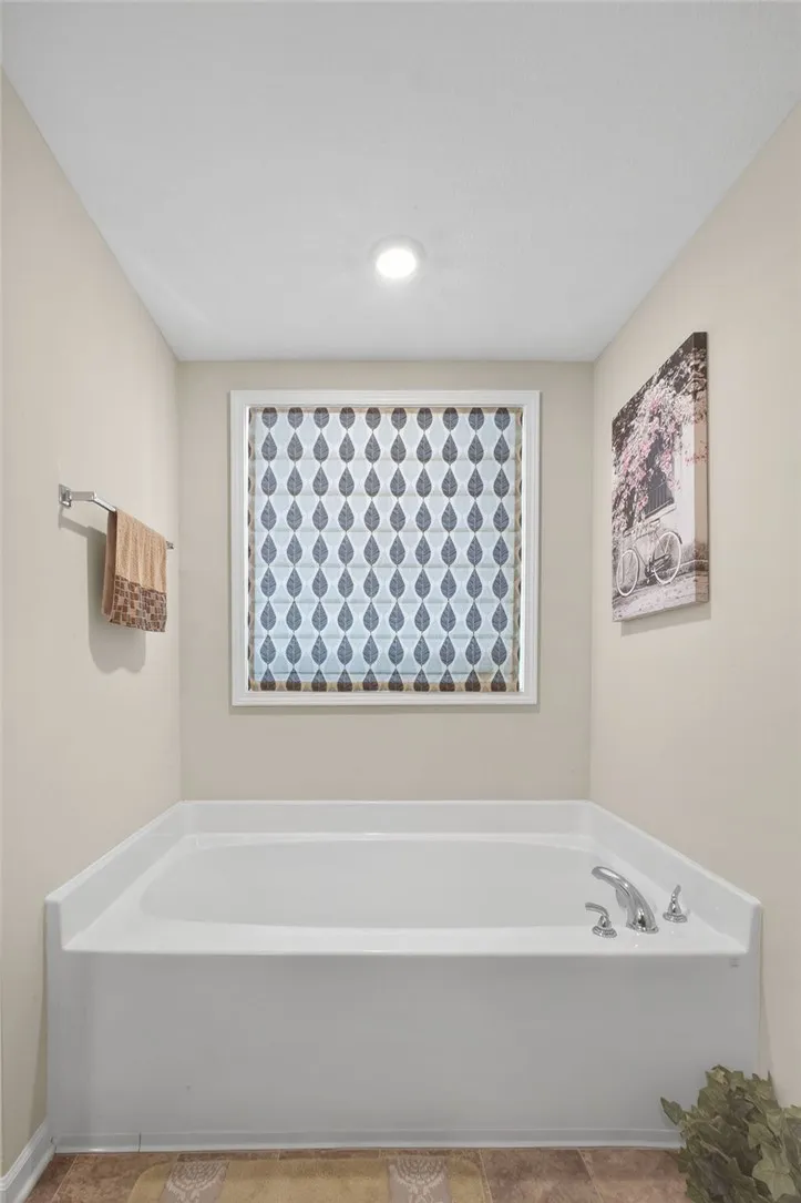 An inviting soaking tub awaits beneath a patterned window, offering a serene escape.