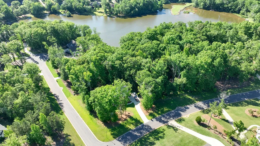 An aerial perspective reveals a winding driveway nestled among mature trees, bordering a tranquil lake.